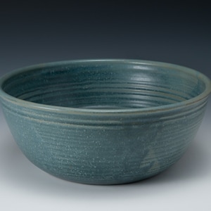 May include: A large, deep, blue-green ceramic bowl with a textured, slightly speckled glaze. The bowl has a rounded shape and a wide rim.