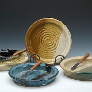 May include: Four ceramic serving dishes with wooden spreaders. The dishes are in various colors and patterns, including black, white, brown, blue, and green.