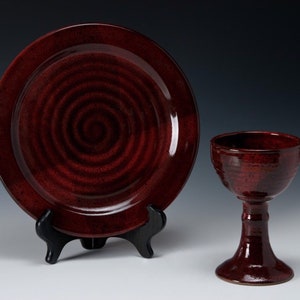 May include: A dark red ceramic plate with a swirling pattern and a matching dark red ceramic chalice.