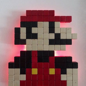 May include: A pixelated wooden wall art sculpture of the iconic video game character, Super Mario. The sculpture is made of individual wooden blocks painted in red, black, and yellow. The sculpture is lit from behind with red LED lights.