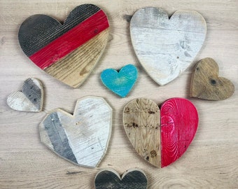 May include: A collection of seven wooden hearts in various colors and patterns. The hearts are painted in shades of red, black, white, and blue. The hearts are arranged in a semi-circle on a wooden surface.