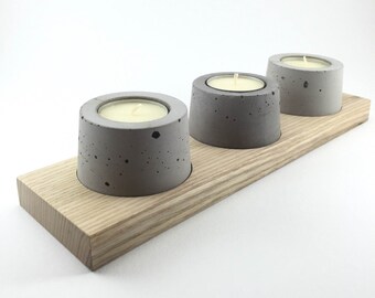 May include: Three gray concrete candle holders with white tea lights, sitting on a wooden tray.