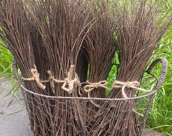 May include: A wire basket with two handles contains several bundles of thin, dark brown twigs. Each bundle is tied together with a piece of light brown twine. The basket is constructed from a thin, gray metal wire mesh.
