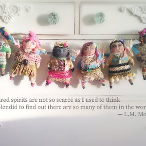 May include: Handmade dolls with wings, each with a unique outfit of colourful fabrics, beads, and lace. They are displayed on a white chest of drawers, with a quote by L.M. Montgomery.
