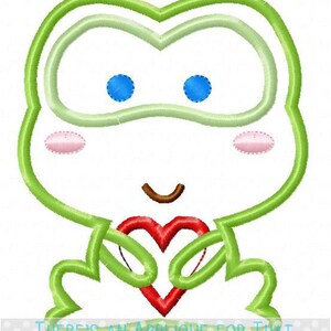 May include: A cartoon frog design with a green outline, blue eyes, and a red heart. The frog is holding the heart with its arms. The text "THERE'S AN APPLIQUE FOR THAT" is at the bottom.