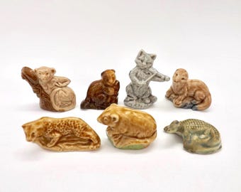 以下が含まれることがあります： さまざまな色の小さなセラミック動物フィギュアのコレクション。 フィギュアには、猿、クマ、猫、ヒョウ、ワニが含まれます。 フィギュアは白い背景にあります。