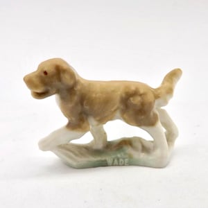 May include: A ceramic dog figurine in shades of brown and white, with red eyes. The dog is standing on a light green base, with the name "WADE" printed on it. This decorative item is likely a collectible figurine.