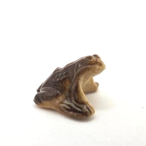 Peut inclure: Petite figurine de grenouille en céramique, dans des tons marron et beige. La grenouille est assise, les pattes avant tendues. La figurine présente des détails soignés et une finition brillante, idéale pour collectionner ou décorer.