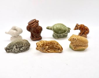 以下が含まれることがあります： アヒル、クマ、カメ、クマ、ハリネズミ、ヒョウ、ヒツジなど、小さなセラミック製の動物フィギュアのコレクション。 フィギュアは茶色、緑、ベージュなどのさまざまな色で、白い表面に配置されています。