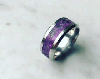Puede incluir: Un anillo de plata con una incrustación de color púrpura de amatista triturada. El anillo es ancho y tiene un acabado pulido.