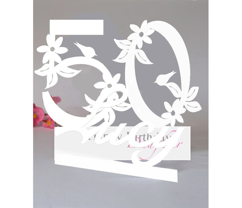 May include: White paper cut-out of the number 50 with floral designs and birds. The number is attached to a white card with the text "Happy Birthday" in cursive.