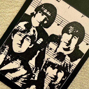 May include: Black and white image of four musicians on a black wooden tag with a string attached. The musicians are silhouetted against a background of sheet music.