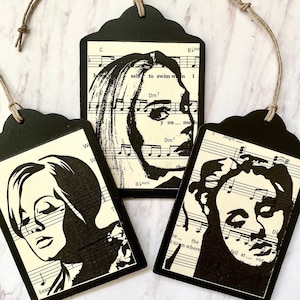 May include: Three black and white silhouette portrait gift tags with a musical note background. The tags are made of wood and have a string attached for hanging. The text on the tags includes "self to swim won", "y on me, b", and "fell at our".