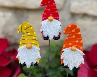 May include: Three colorful gnomes with white beards and black shoes. The gnomes are painted with polka dots and stripes in red, yellow, and orange.