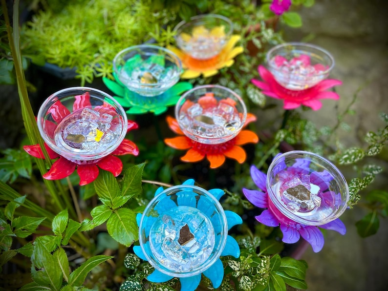 May include: Seven colorful flower-shaped hummingbird feeders with clear glass cups. The feeders are made of plastic and have a bright, cheerful design.