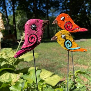 May include: Three colorful ceramic bird figurines with gold accents and painted details. The birds are on black metal stakes and are arranged in a row.