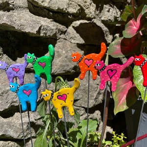 Puede incluir: Siete estacas de jard&iacute;n de gato de colores con corazones y lunares. Los gatos est&aacute;n hechos de arcilla pintada y est&aacute;n unidos a estacas de metal. Las estacas se insertan en el suelo.