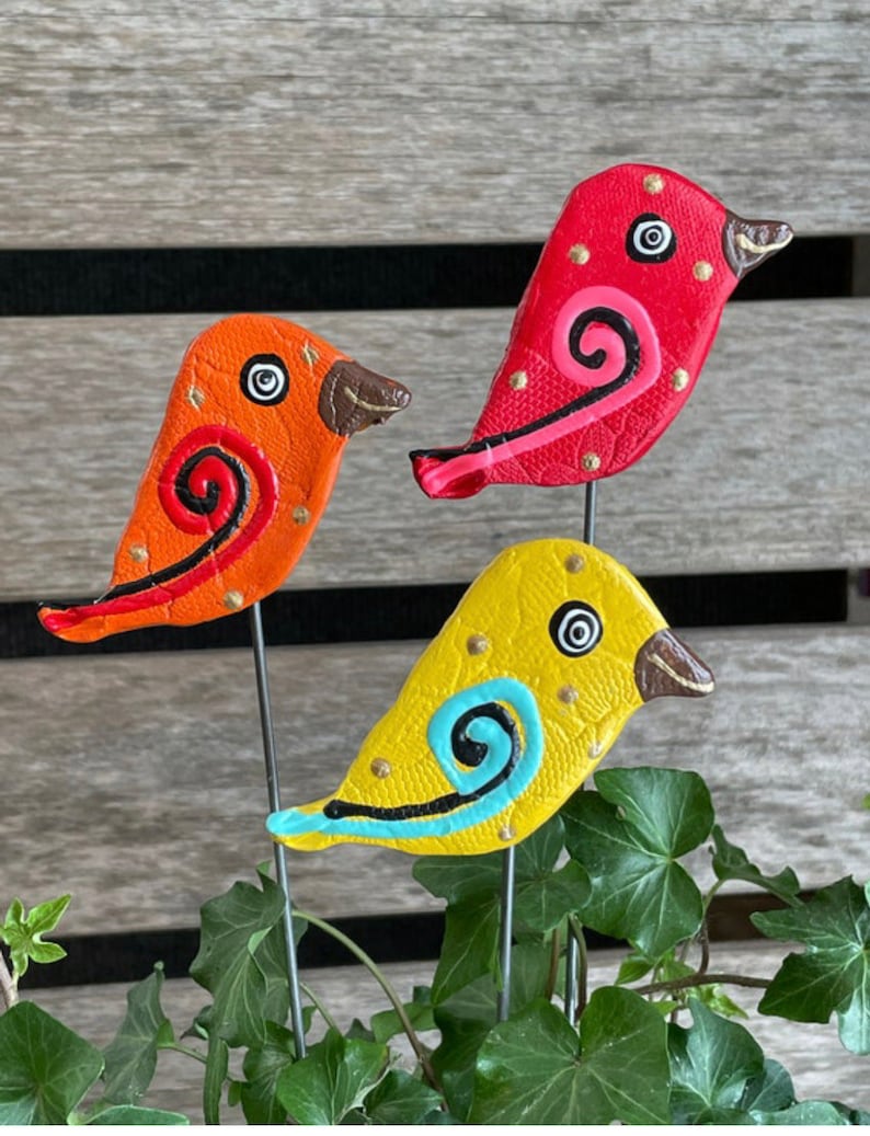 May include: Three colorful ceramic bird figurines with painted details, each with a wire stem. The birds are orange, red, and yellow with black and white eyes and a swirl design.