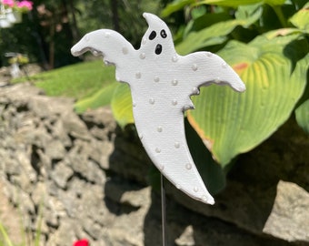 May include: A white ghost with black eyes and a white polka dot pattern. The ghost is attached to a metal stake.