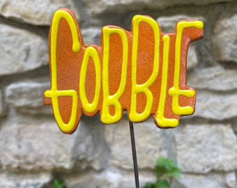 May include: A terracotta-colored garden stake with the word "Cobbie" written in yellow paint.