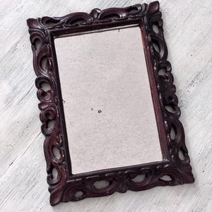 Peut inclure: Miroir rectangulaire avec un cadre orné bordeaux foncé. Le cadre présente un motif tourbillonnant détaillé. La surface du miroir est de couleur gris clair et le cadre a un aspect légèrement vieilli.
