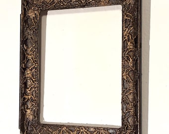 May include: Ornate rectangular picture frame with a dark brown finish and gold accents. The frame has a detailed, textured design around the edges. The frame is empty, ready for a photo or artwork.