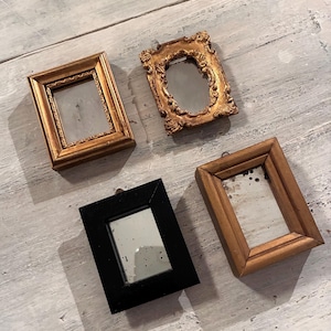 Può includere: Quattro piccole cornici ornate nei toni dell'oro, del nero e del marrone. Le cornici hanno un'estetica vintage, con dettagli intricati e specchi invecchiati. Le cornici sono rettangolari e quadrate, con una varietà di bordi decorativi.