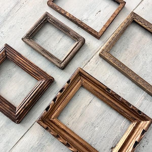 May include: A collection of rectangular picture frames in different sizes and styles. The wooden frames have various finishes, including dark brown, gold, and distressed textures. Some frames feature decorative details.