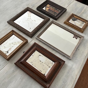 Può includere: Collezione di specchi antichi con cornici decorative ornate di varie dimensioni e forme. Le cornici sono in legno e metallo, con colori che vanno dal marrone scuro all'oro e all'argento. Gli specchi hanno superfici invecchiate e usurate.