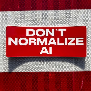 May include: A rectangular red sticker with rounded corners featuring the white text DON'T NORMALIZE AI in a bold, sans-serif font. The sticker is positioned against a background with a white and red diamond-patterned reflective surface.