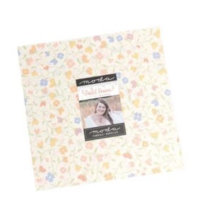 May include: A square fabric bundle with a floral pattern in pastel colors. The fabric features small flowers in shades of pink, yellow, and blue on a cream background. A label with the text "Pastel Prairie" and a woman's image is attached.