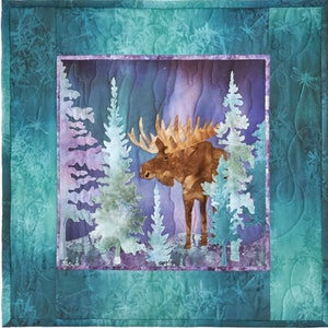 May include: A square fabric wall hanging featuring a central panel with a brown moose standing among light blue and white evergreen trees against a purple and blue background. The border is a teal fabric with a subtle dragonfly pattern.