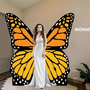 May include: A woman in a white dress stands in front of a large monarch butterfly wing graphic. The graphic is on a wall with the word "MONARCH" printed on it.