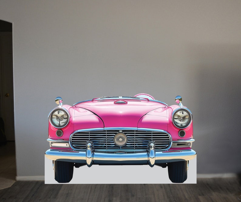 May include: A pink vintage car with chrome accents and a chrome grill. The car is facing forward and the headlights are on.