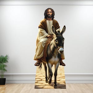 May include: A cutout of a man with dark skin riding a donkey. The man is wearing a brown robe and has a long beard. The donkey is brown and white and has a saddle. The background is a stone path.