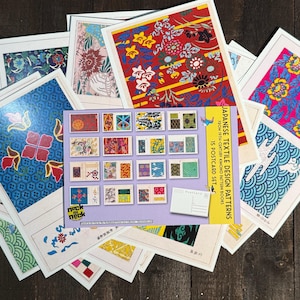 May include: A collection of postcards featuring Japanese textile designs. The postcards showcase various colorful patterns, including floral and geometric motifs. A set of 15 postcards is visible, with the text "Japanese Textile Design Patterns" on the packaging.