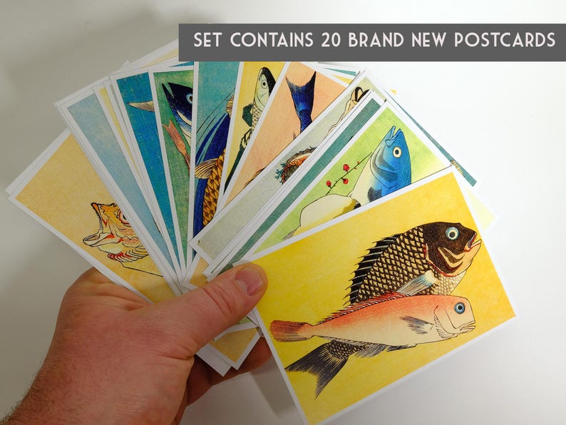 May include: A set of 20 brand new postcards featuring colorful illustrations of fish. The postcards are held in a hand, fanned out to show the different designs.  The text "SET CONTAINS 20 BRAND NEW POSTCARDS" is printed at the top of the image.