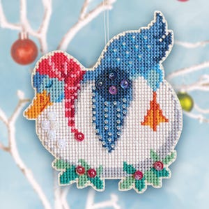 May include: A handmade Christmas ornament shaped like a bird, featuring cross-stitch embroidery. The bird has a blue body, a red and white hat and scarf, and is decorated with beads. A small orange tree is stitched on the bird's body.