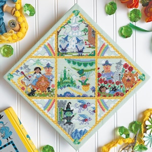 May include: A diamond-shaped cross-stitch piece depicting scenes from the Wizard of Oz. The scenes include Dorothy and Toto, the Wicked Witch of the West, the Emerald City, and the Wizard.