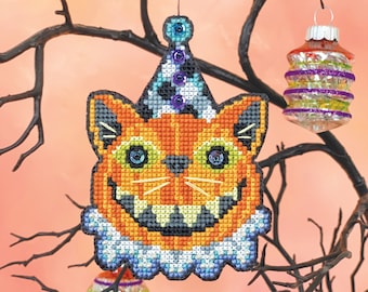 May include: A Halloween-themed cross-stitch ornament featuring a grinning orange cat wearing a blue and white party hat. The cat has green eyes and a white ruff. The ornament is hanging from a branch.
