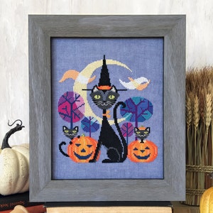 May include: Cross-stitch artwork in a grey frame, depicting a black cat in a witch's hat, flanked by two carved pumpkins. The background shows a crescent moon, trees, and small black cats. Ideal for Halloween, this piece is a charming addition to any home.