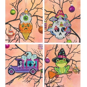 Könnte beinhalten: Vier Halloween-Kreuzstich-Ornamente. Designs umfassen eine Eistüte mit einem Auge, einen Totenkopf mit einem Pilzhut, einen lila Leichenwagen mit Geistern und einen Frosch auf einem Besen. Jedes Ornament hängt an einem schwarzen Ast mit dekorativen Kugeln.