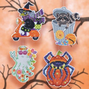 May include: Four hanging cross-stitch ornaments featuring Halloween themes: a witch on an orange scooter, a raccoon in a trash can with candy, a ghost wearing flower crown and glasses, and a spider with a pumpkin body, all with small embellishments.