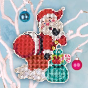 May include: A cross-stitch Christmas ornament depicting Santa Claus in a red suit with a white beard and a sack of gifts. The ornament is embellished with beads and has a string for hanging. The background features a blue sky and decorative ornaments.