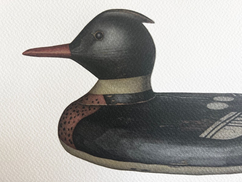 May include: A black and brown wooden duck decoy with a red beak. The duck has a white band around its neck and a detailed pattern on its body.