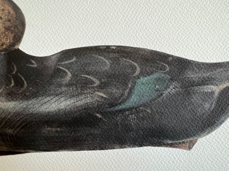 May include: Close-up of a black and gray duck decoy with a teal blue fish design on the side.
