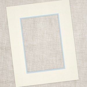 Op de afbeelding: Een gebroken witte passe-partout met een rechthoekige opening en een lichtblauwe rand. De passe-partout is geplaatst tegen een neutrale, getextureerde achtergrond, wat een strakke en eenvoudige esthetiek creëert. Ideaal voor het inlijsten van foto's of kunstwerken.