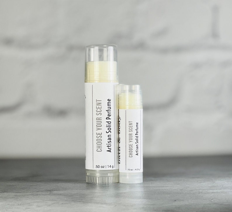 May include: Two white tubes of solid perfume with the text "Choose Your Scent Artisan Solid Perfume" and the size in ounces and grams. The larger tube is 50 oz | 14 g and the smaller tube is 15 oz | 4.25 g.