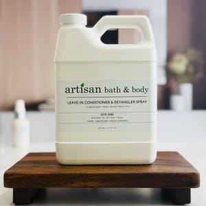 May include: A white Artisan Bath & Body leave-in conditioner and detangler spray bottle with a handle. The label reads "Leave-in Conditioner & Detangler Spray" and "Suitable for All Hair Types." The bottle is 847 ml / 32 fl oz.