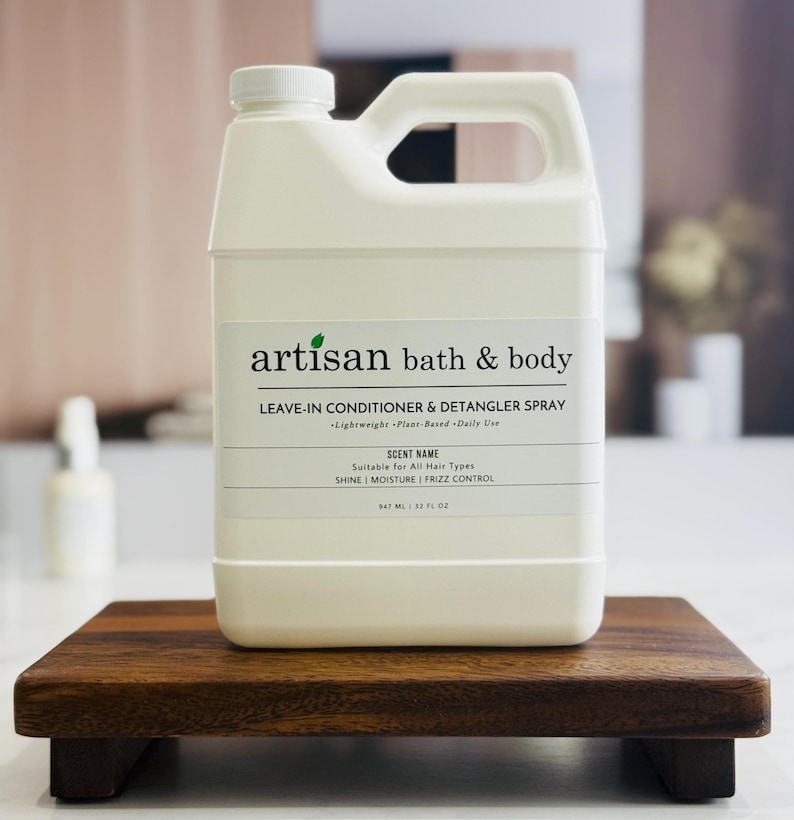 May include: A white Artisan Bath & Body leave-in conditioner and detangler spray bottle with a handle. The label reads "Leave-in Conditioner & Detangler Spray" and "Suitable for All Hair Types." The bottle is 847 ml / 32 fl oz.